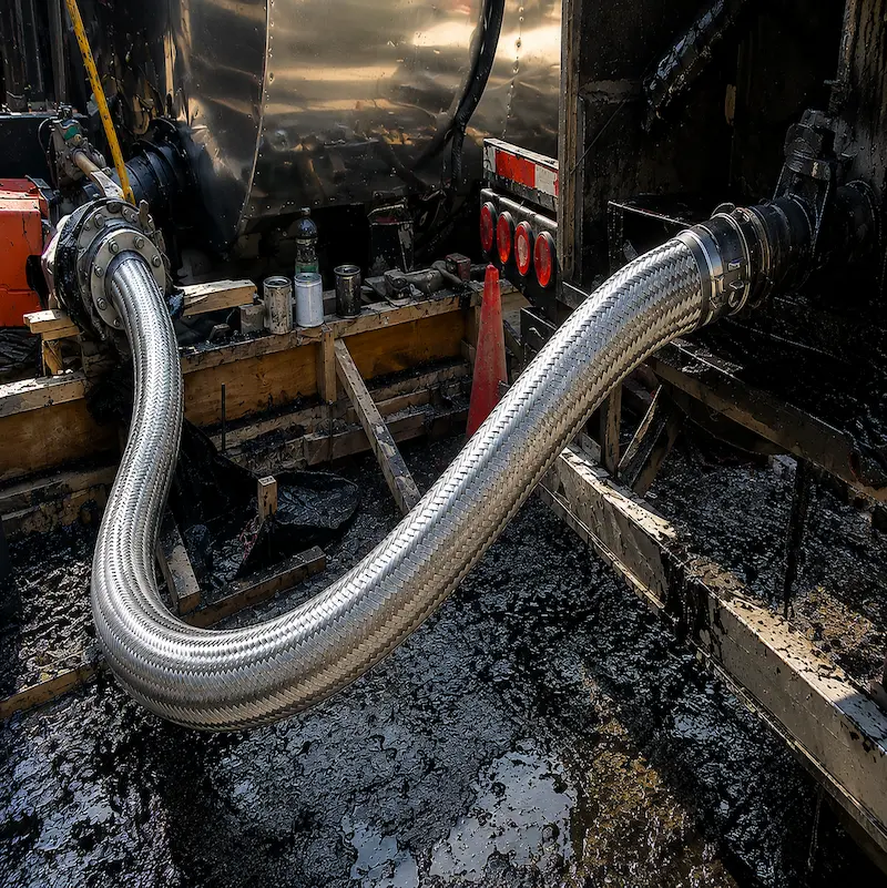 Manguera metálica flexible para asfalto y bitumen en acero inoxidable, instalada en equipo industrial para transferencia de fluidos calientes.